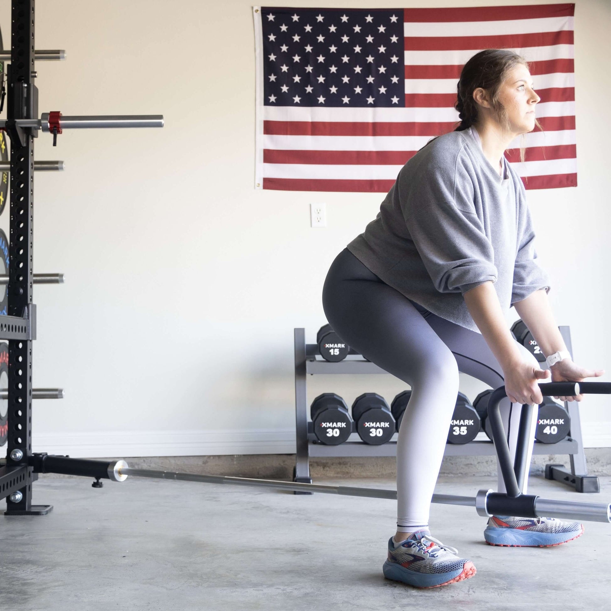 Woman using Viper landmine attachment for workout in garage, with American flag in background and dumbbells visible.