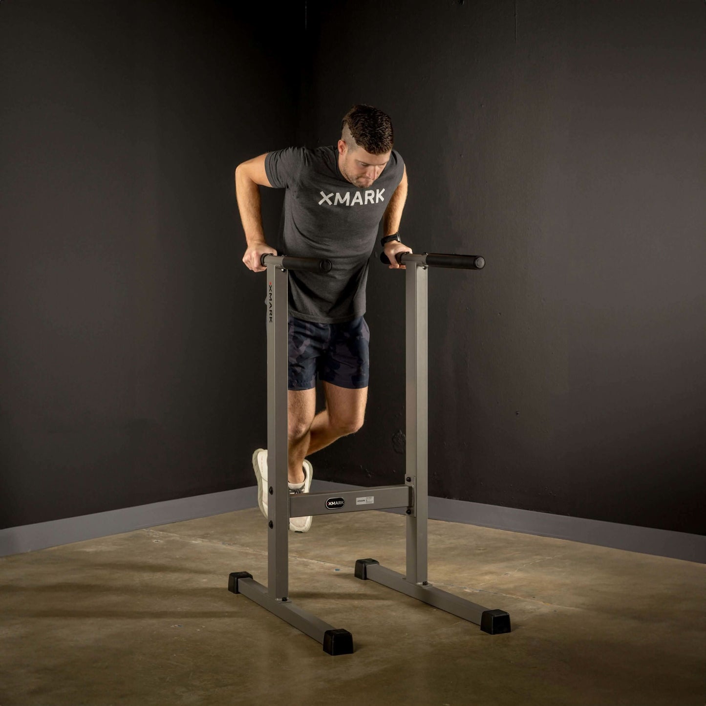 A person performing dips on the XMARK Dip Stand Station, showcasing upper-body strength training in a gym setting.