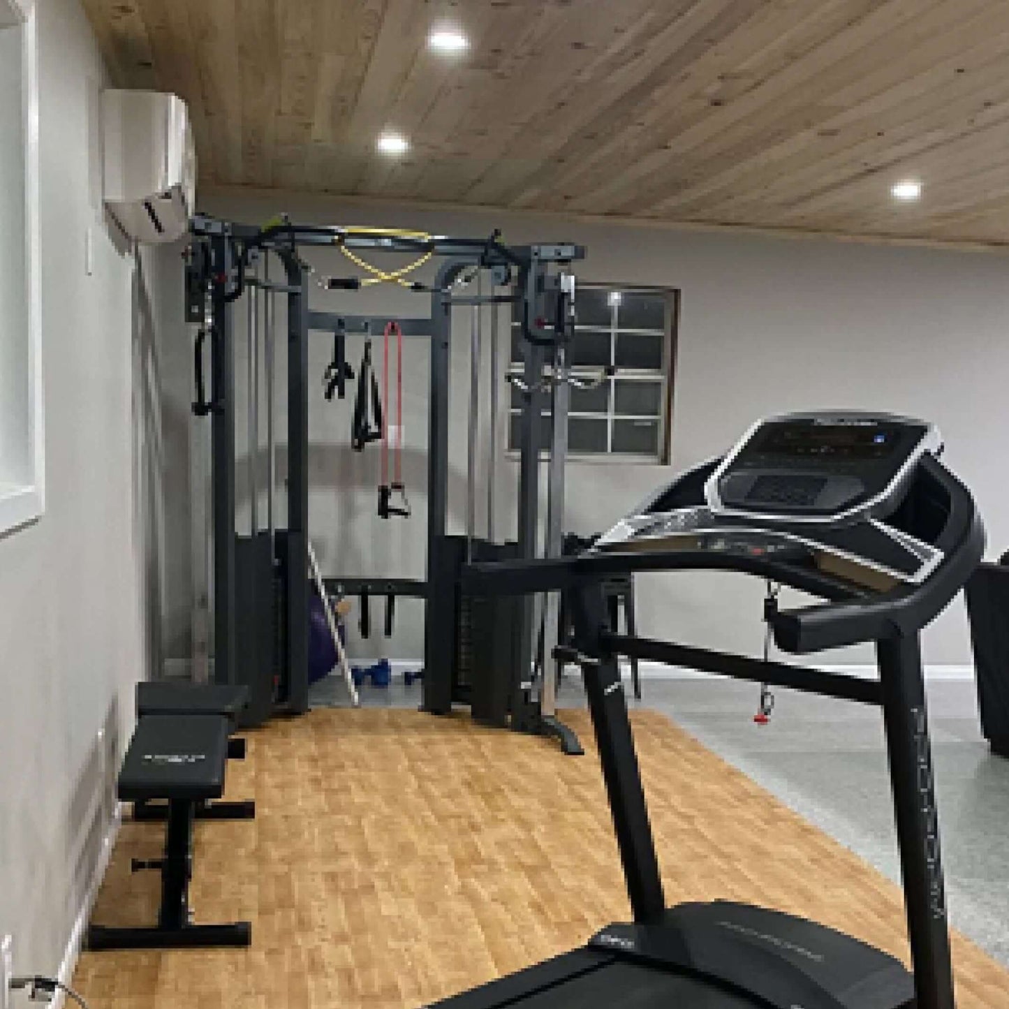 Home gym with a functional trainer cable machine, treadmill, and adjustable bench for versatile workouts.